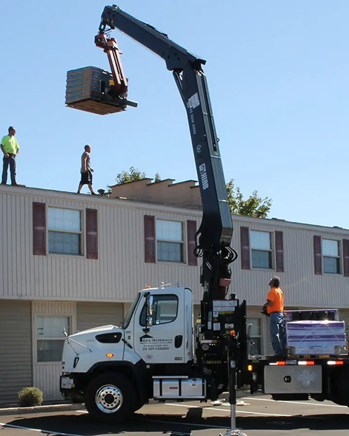 Workers operating a crane lifting materials onto the roof of a building